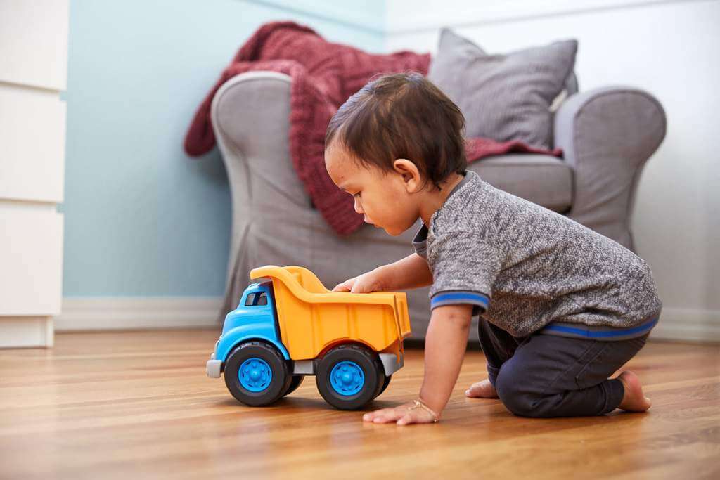 Toddler playing with eco-friendly Blue & Orange Dump Truck made from recycled plastic in a cozy living room.