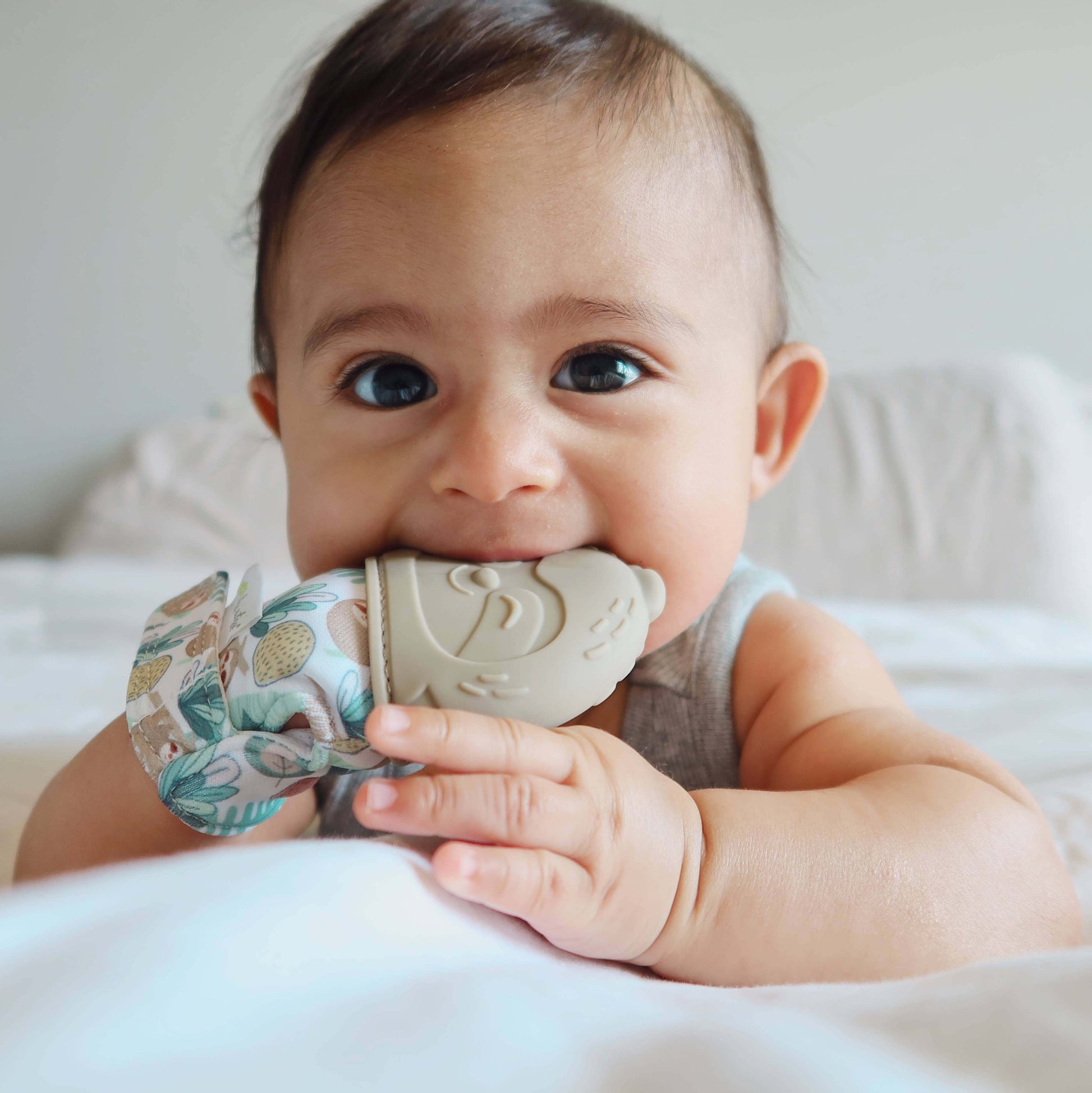 Baby chewing on Itzy Mitt™ Silicone Teething Mitt with fox design for soothing sore gums, wearing it like a glove in bed.