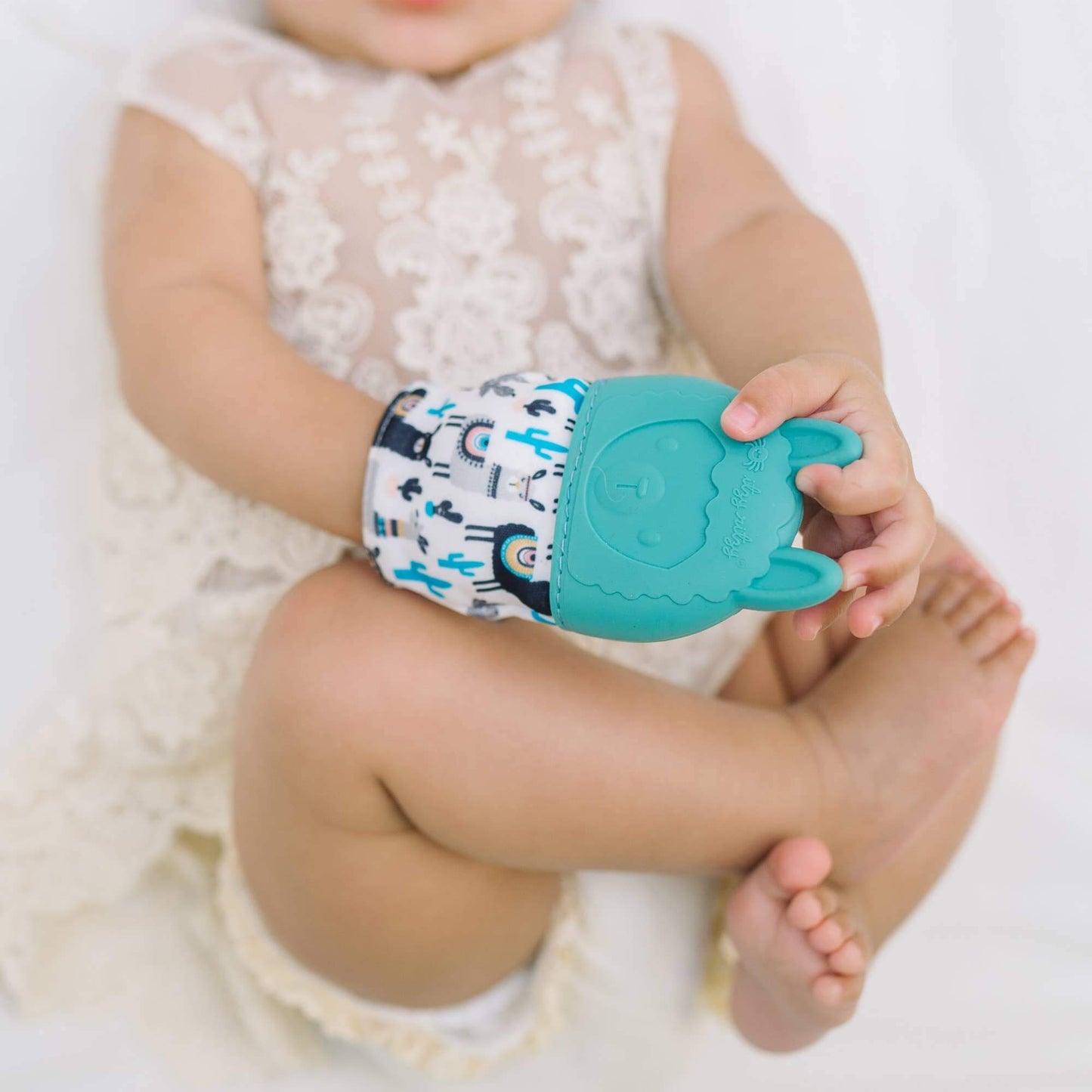 Baby wearing Itzy Mitt™ Silicone Teething Mitt in Sloth design, holding the turquoise mitt with detailed texture and playful print