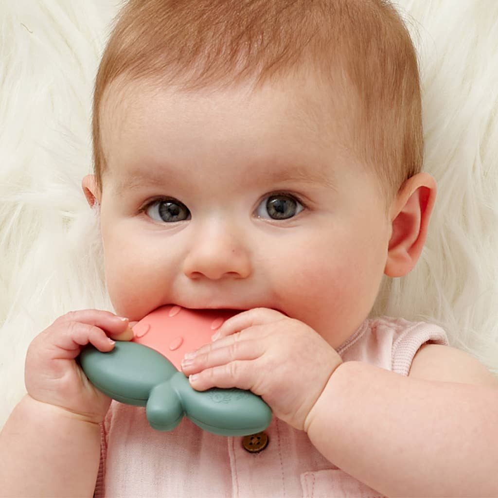 Baby using Strawberry Sweetie Rattle™ silicone teether with multiple textures to soothe sore gums.