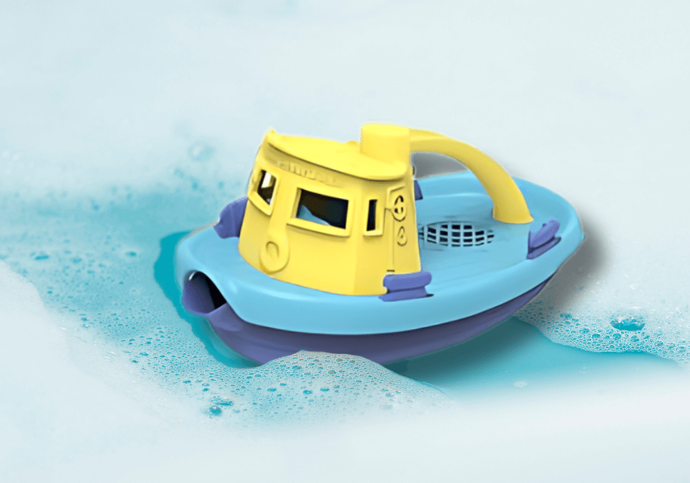 Brightly-colored Green Toys Tugboat made from 100% recycled ocean bound plastic floating in soapy water, perfect for bathtub play.