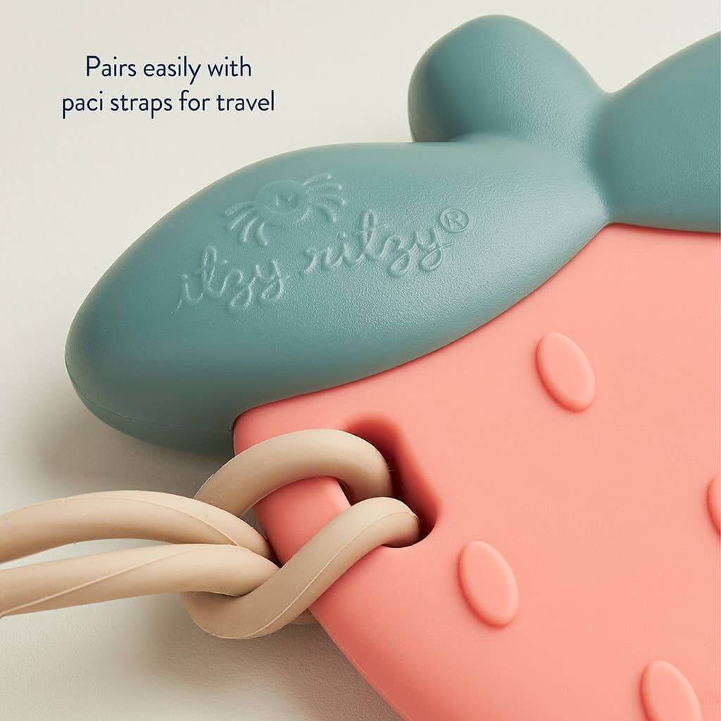 Close-up of Strawberry Sweetie Rattle™ silicone teether with paci straps, showing soft flexible texture and travel-friendly design.