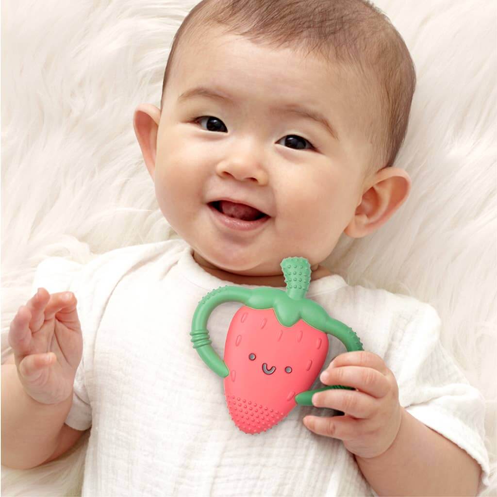 Baby holding Bonnie the Strawberry teether, part of Itzy Ritzy's Chew Crew collection, designed to soothe sore gums with soft silicone.